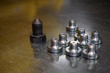 One large gray screw plug next to a lot of small shiny blurry plugs on a steel background. Big and small concept.