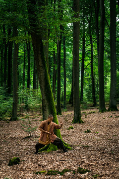 Asian guy in brown uniform gesticulating while doing martial arts exercise during workout in green forest