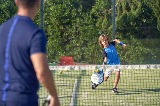 Boy in sportswear waiting for coach passing ball while playing paddle tennis on court during training