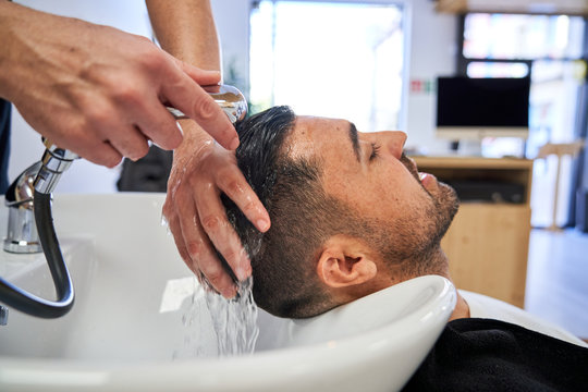Stock photo of a boy with his head reclining on the pica of a barbershop while they wash his head with water. Barbershop