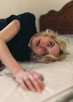Pretty young blond freckled female with brown eyes in casual black shirt looking away and contemplating while resting in bed