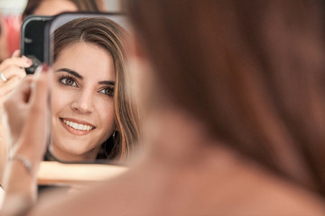 Reflection of a beautiful woman face in mirror in hand of smiling lady after cosmetic procedure in salon