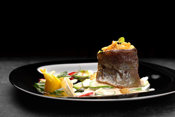 Grilled trout fillet with vegetables, on black background