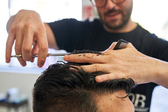 Stock photo of a detail of a hand from a barber cutting hair with scissors and a comb to a customer with the blur in the background
