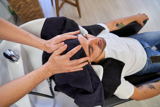 Stock photo of a man seated with his head in the pile of the hairdresser and a few hands that dry head with a towel