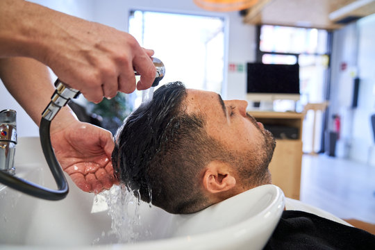 Stock photo of a boy with his head reclining on the pica of a barbershop while they wash his head with water. Barbershop