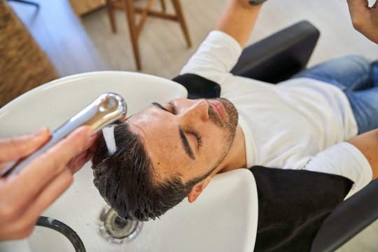 Stock photo of a boy with his head reclining on the pica of a barbershop while they wash his head with water