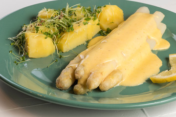 white asparagus poured with .hollandaise sauce, potatoes with chives and sprouts.