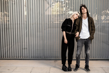 Side view of trendy couple supporting each other while woman leans on boyfriend against striped wall of modern building