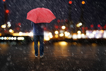 Person mit Regenschirm steht vor den Lichtern einer Stadt