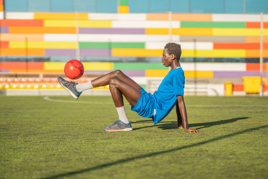 Side view of ethnic football player leaning back and juggling ball on foot during workout on stadium