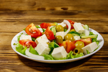 Greek salad with fresh vegetables, feta cheese and green olives on wooden table