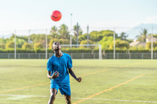 Skinny black teenager jugging football ball on head