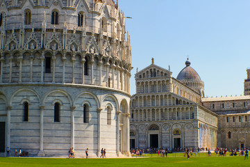 view of the baptistery of Pisa and behind the cathedral during a sunny day