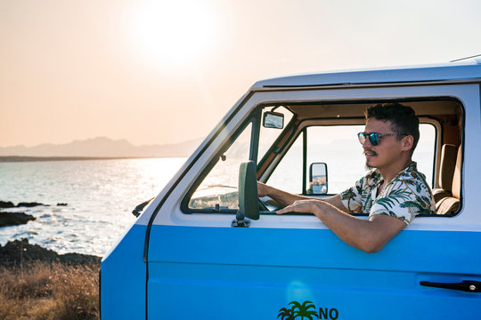 Side view of adult male in sunglasses and casual clothes looking away in contemplation while sitting alone in parked blue van on beach
