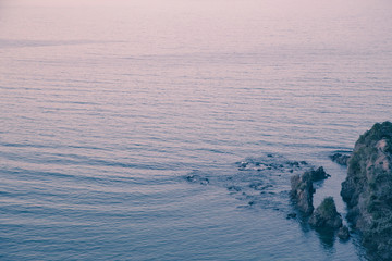 Close up of rocky reef at sunrise. Beautiful muted pink tones. Pacific ocean. Ripples on water, small swell at surf beach. Sandy Bay, Northland, NZ. Copy space, minimalist look. Feels peaceful, calm