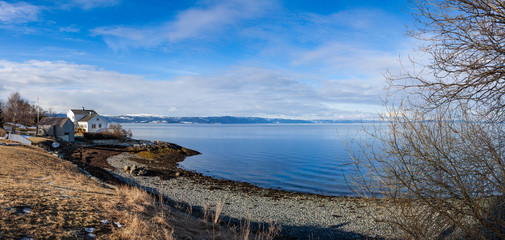 White Scandinavian house by the water with fjords in the background. Norway in Europe. High-quality panoramic photo. A sunny winter day