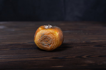 a completely rotten apple lies on a wooden table. a spoiled apple is black on one side and brown on the other. mold and fungi spread throughout the fruit
