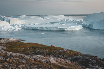 Fototapeta na wymiar vening scene in Ilulissat with view towards Kangia Icefjord with tent and floating icebergs on an overcast day