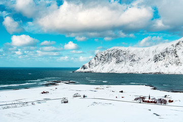 Top view of a Norwegian village covered with snow near the sea. Behind it is a snow rock. Lofoten Islands