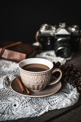 Hot coffee with cinnamon sticks, cookies and vintage camera on a wooden background