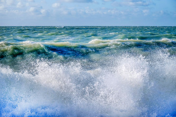 White sea spray of a wave breaking on the beach with a rough sea and sky behind