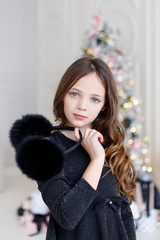 Little girl in fur headphones and black dress. Beautiful little girl with long blonde hair wearing black fur headphones.  Little Girl in a Fur Headphones.  Merry Christmas and Happy New Year.