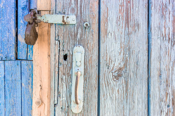 open padlock on a scuffed wooden door with weathered cracks of blue and beige colors of old country house