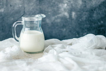Glass carafe of fresh milk on a wooden white table with white fabric