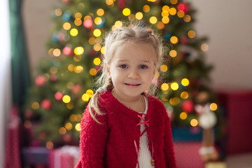 Portrait of a happy pretty girl at the Christmas tree, waiting for the new year