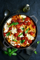 Pasta casserole with tomatoes and mozzarella cheese in a cast iron pan. Top view with copy space.