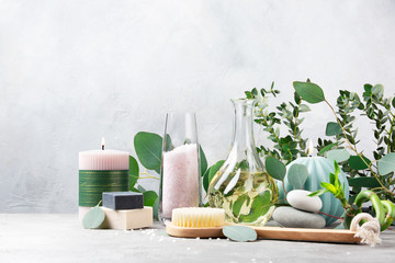  Spa and bath concept. Oil for body massage, lavender sea salt, body brush, candles, fresh bamboo, soap with scrub, black soap with coal and branches of eucalyptus on light grey table. Copy space.