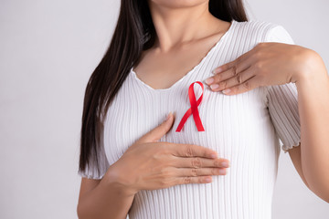 Closeup of woman hand pointing to red badge ribbon on chest to support AIDS Day. Healthcare, medicine and AIDS awareness concept.