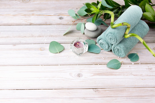 Spa and bath concept. Light turquoise towels, fresh bamboo, candle, sea stones and eucalyptus leaves on a light old wooden background. Copy space