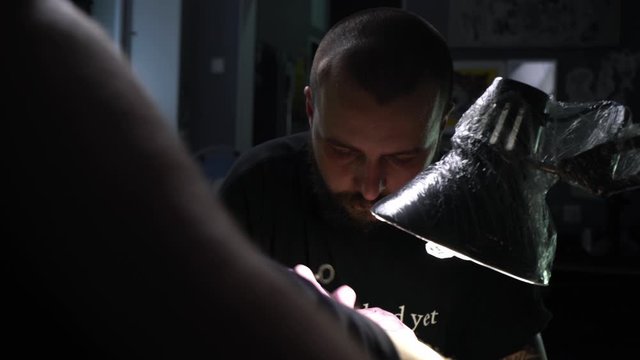 Blackwork in tattoo studio. Tattoo master makes a tattoo on a man's leg. The artist with a beard and pink gloves makes a tattoo of white paint on a black. Individuality. Be unique. White and black.