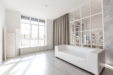 Bright, minimalist living room interior with white sofa stands near the window