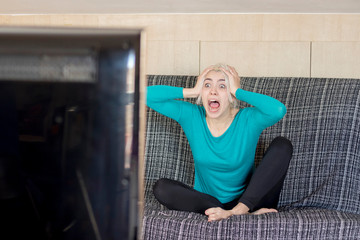 beautiful young surprised woman watching TV at home alone.