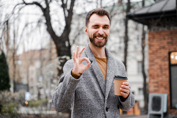 Portrait of a smiling mature businessman dressed in coat showing ok gesture. People sincere...