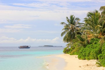 Amazing beautiful deserted beach with coconut palm trees on tropical island in Indian ocean.Traditional local longtail ship for sea excursuon and blurred island resort with bungalows on background.