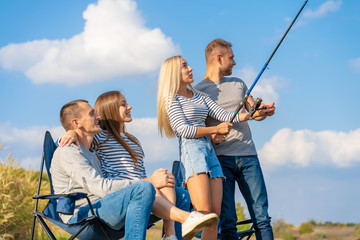 Group of young friends fishing on the pier by lakeside