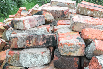 Many old used broken dirty burnt bricks with remnants of cement are stacked in rows on the grass in garden