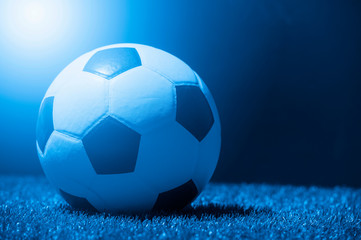 Soccer ball on grass against black background. Blue filter
