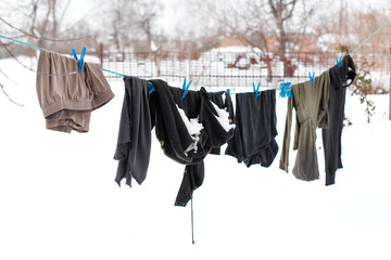 Winter. Clothes are drying on the street. Clothes covered with snow dries on a tightened rope.