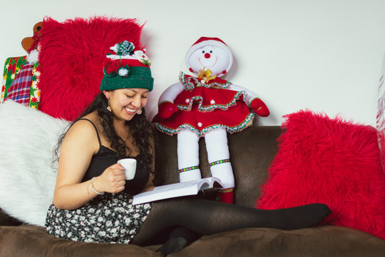 Colombian woman at Christmas sitting on the sofa reading a book and drinking coffee