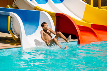 Happy cheerful boy splashing water on water slide at aqua park