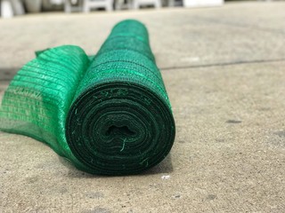 The roll of green shading net is on the concrete floor, it is always used for giving proper climate conditions to the plants.