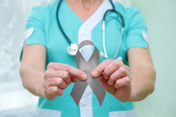 Doctor with stethoscope on his neck, shows a grey ribbon close-up in two hands. Parkinson's disease or brain cancer awareness symbolic concept to help support the campaign against illness