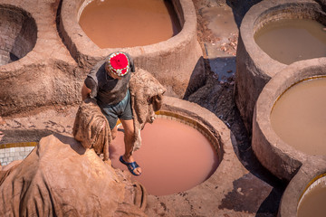 Landscape view of colorful barrels in a tannery in the old medina.  Worker preparing animal skin...