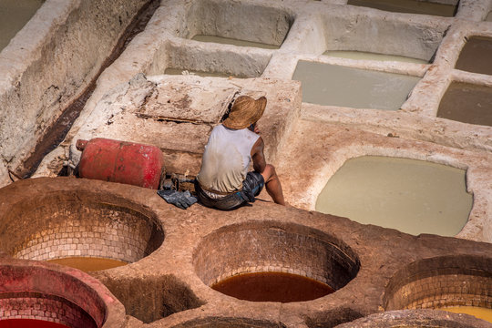 Landscape view of colorful barrels in a tannery in the old medina. Worker sitting on the barrel, resting. Fez, Morocco.