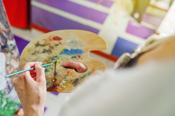 Close up on hands of young woman female painter art holding a painting brush and artist palette with colors painting